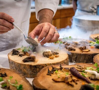 A chef artfully plating a gourmet dish with mushrooms and greens on wood slices.